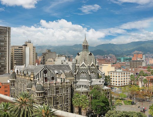 Fachada neogótica ajedrezada del Palacio de la Cultura Rafael Uribe Uribe en Medellín, con cúpula, gárgolas y plaza con fuente y personas al frente.