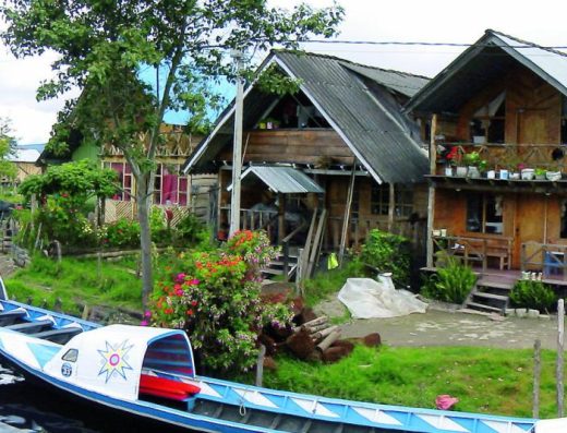 Casas de madera sobre pilotes y botes de colores en el muelle de El Encano, a orillas de la Laguna de la Cocha, rodeada de montañas nubladas en Nariño.