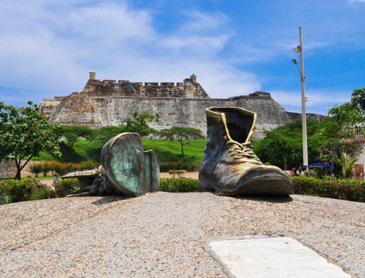 Monumento Zapatos Viejos Cartagena: botas gigantes de bronce gastadas, una vertical y otra recostada, con Castillo San Felipe al fondo