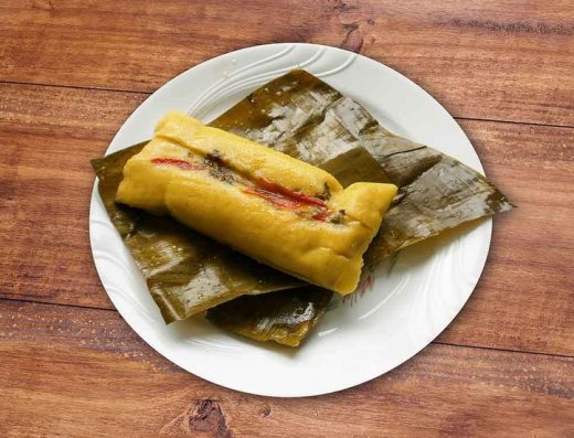 Hallacas llaneras envueltas en hojas de plátano sobre una mesa con ingredientes tradicionales