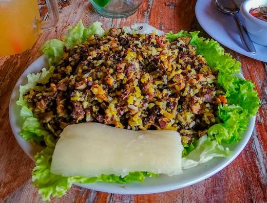 Plato de pepitoria santandereana con arroz, vísceras y arvejas, servido con patacón y yuca sobre hojas de maíz